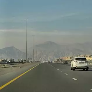 سيارة بيضاء تسير على طريق دبي السريع مع جبال في الخلفية