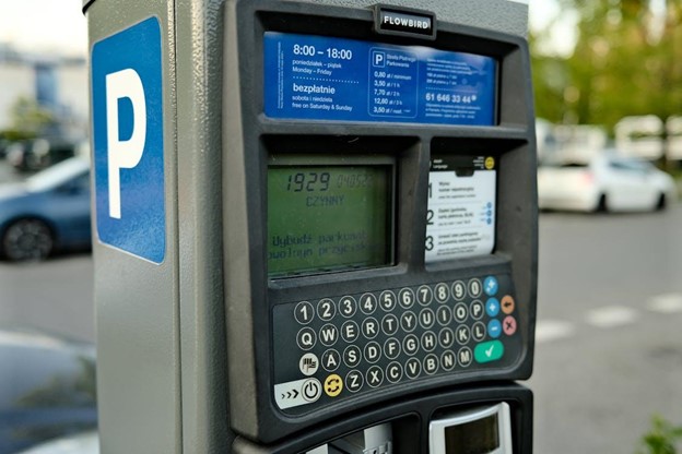 A digital parking meter in a city setting with cars in the background.